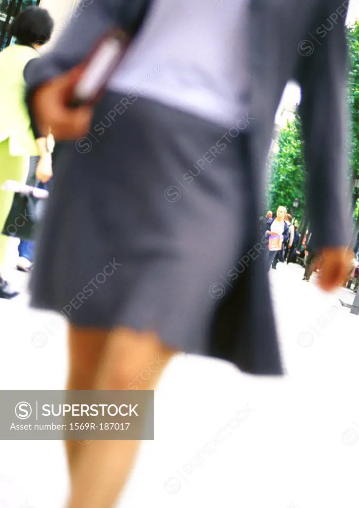 Businesswoman walking with book in hand, close-up, blurred