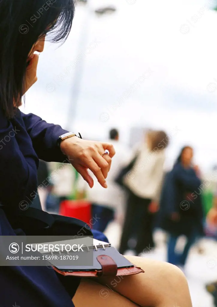 Businesswoman looking at watch, agenda on lap
