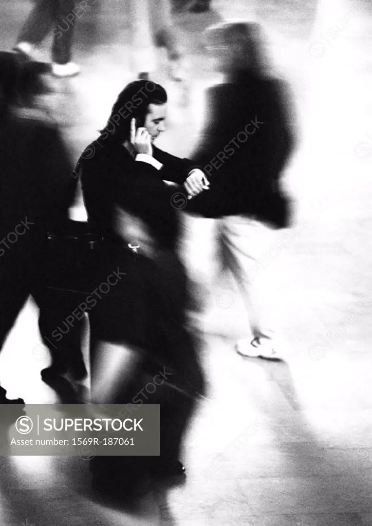 Businessman standing and using cell phone in crowd, blurred motion, b&w