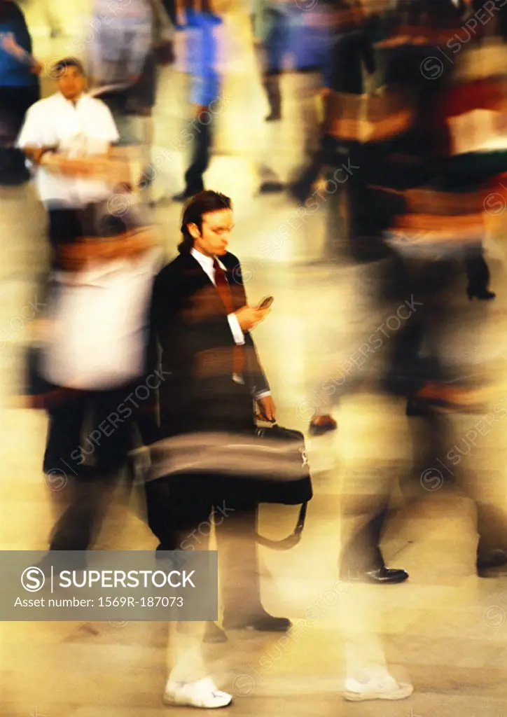 Businessman in blurred crowd, using cell phone, full length