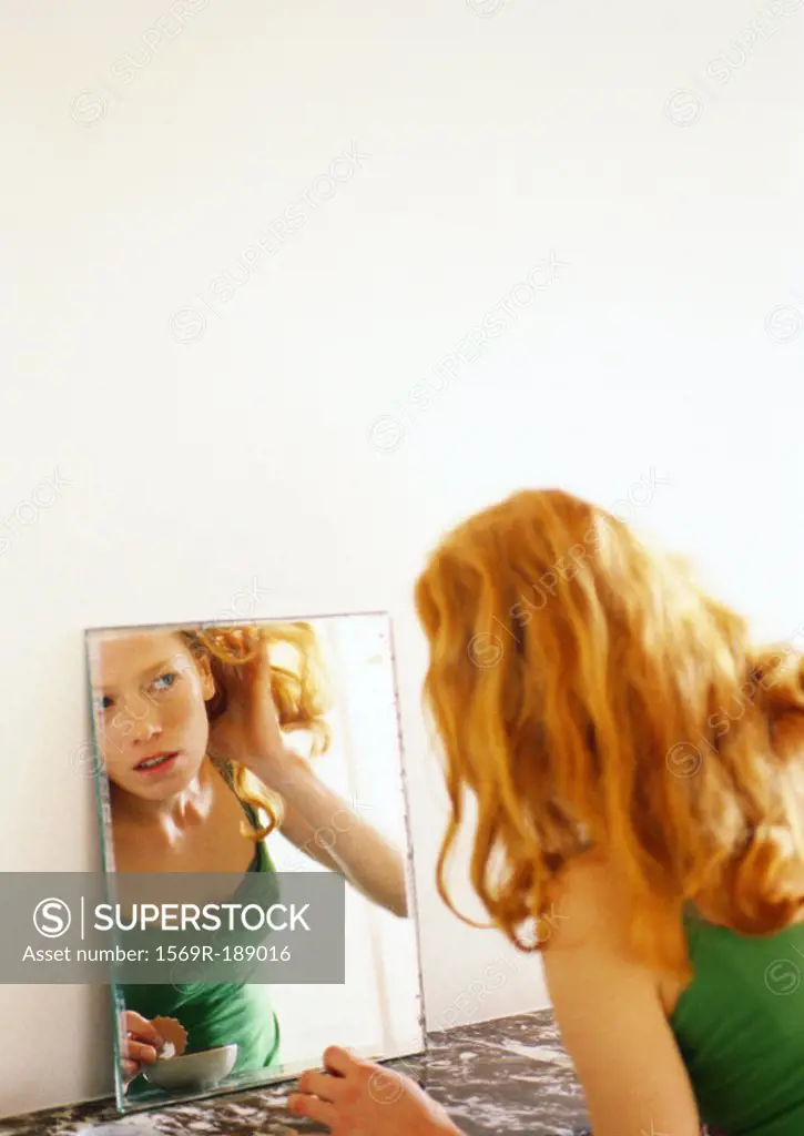Woman looking at reflection in mirror, pulling her hair back