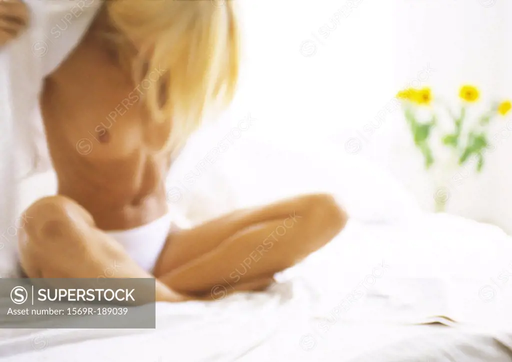 Woman sitting on bed with legs crossed, partially nude, blurred