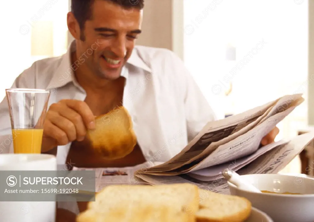 Man sitting reading newspaper, eating breakfast