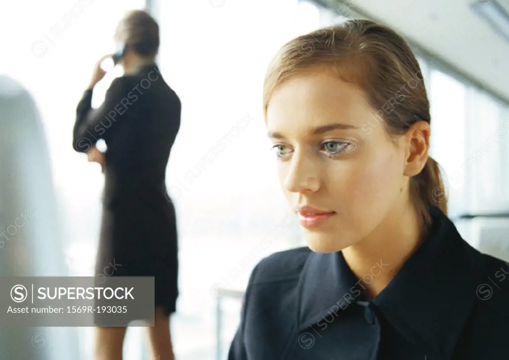 Businesswoman on cell phone, rear view, in background, blurred, businesswoman working in foreground, close-up