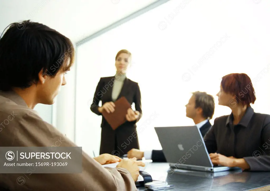 Business people around table looking at businesswoman standing