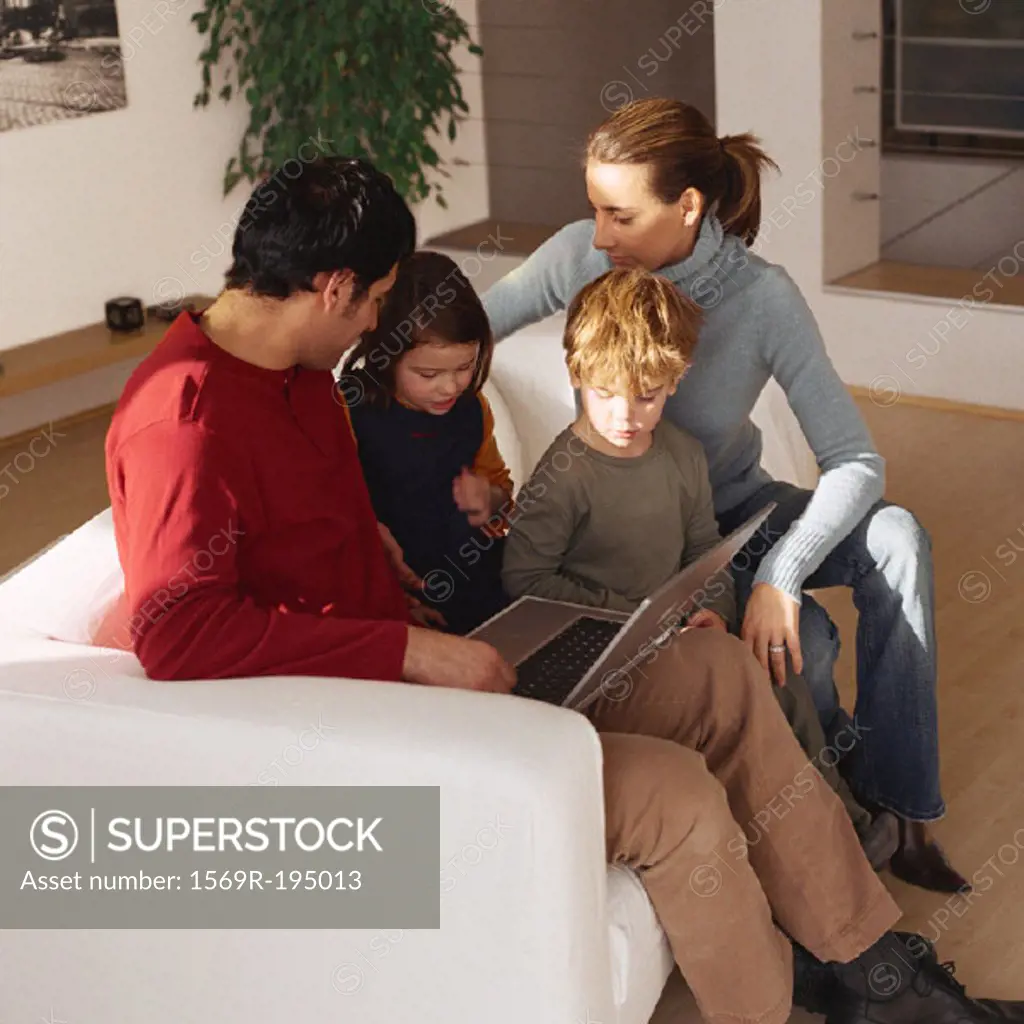 Family sitting together on sofa, looking at laptop