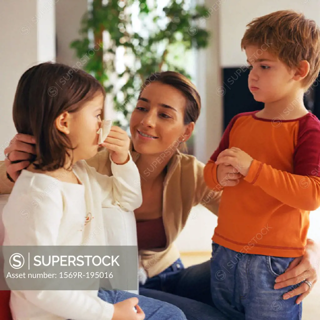 Woman with arms around two children, looking at girl blowing nose