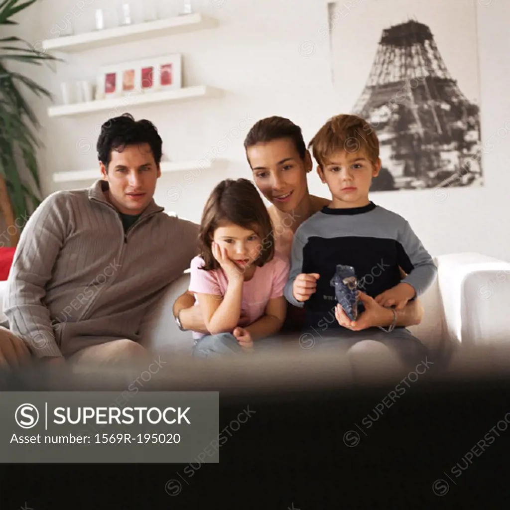 Family sitting on the couch, rear view of tv in foreground, blurred