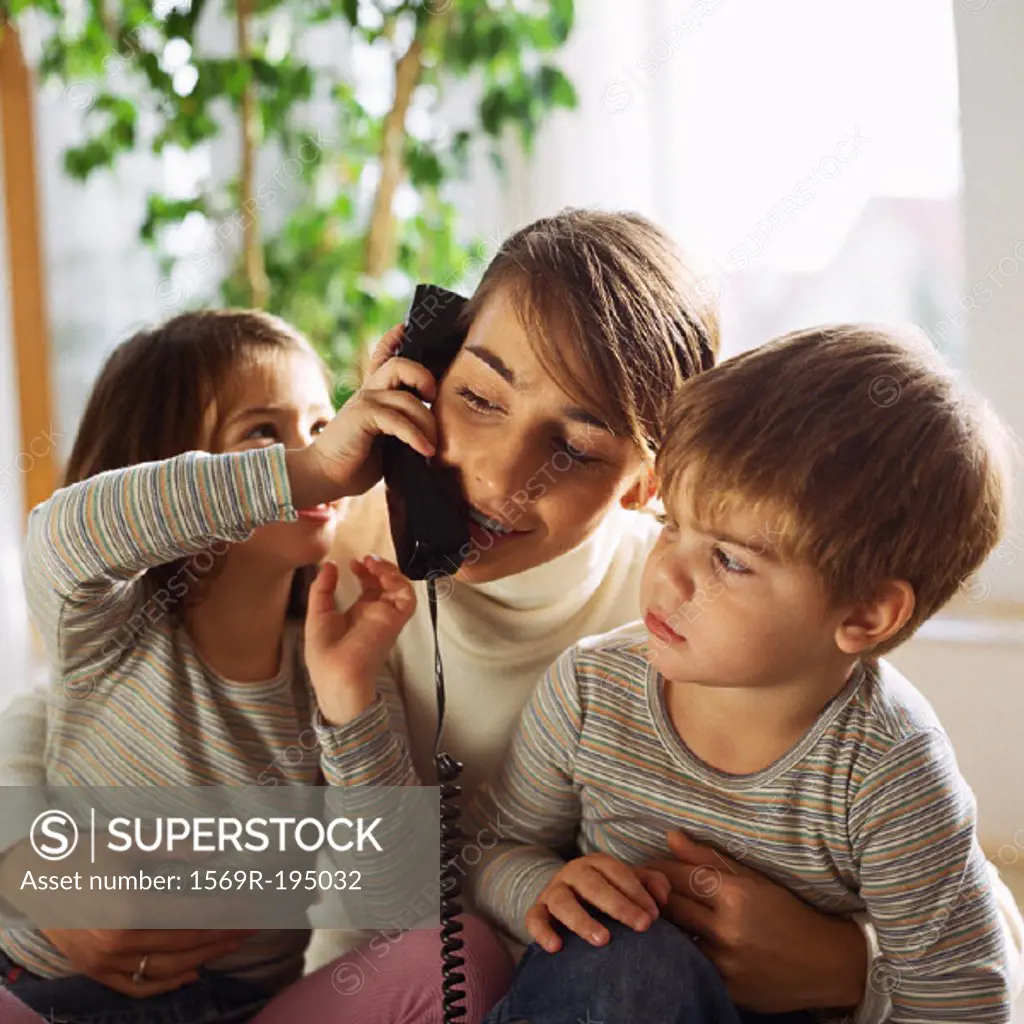 Mother sitting with children, daughter holding phone to mother´s ear