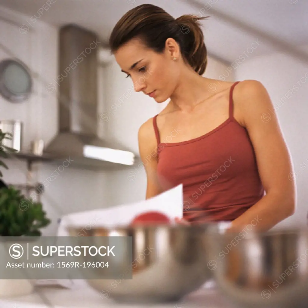 Woman working in kitchen, waist up, bowls on counter in foreground, blurred