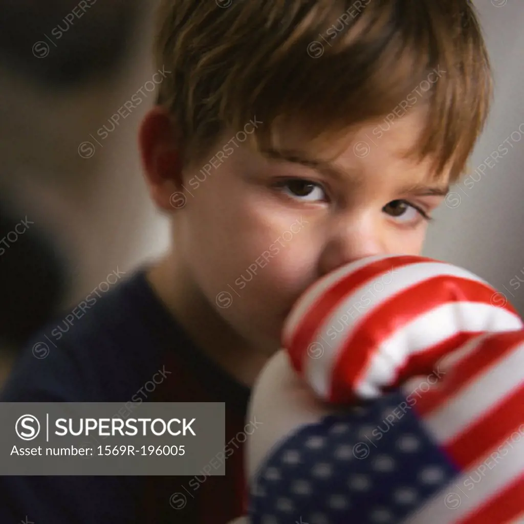 Young boy covering mouth with boxing gloves, portrait