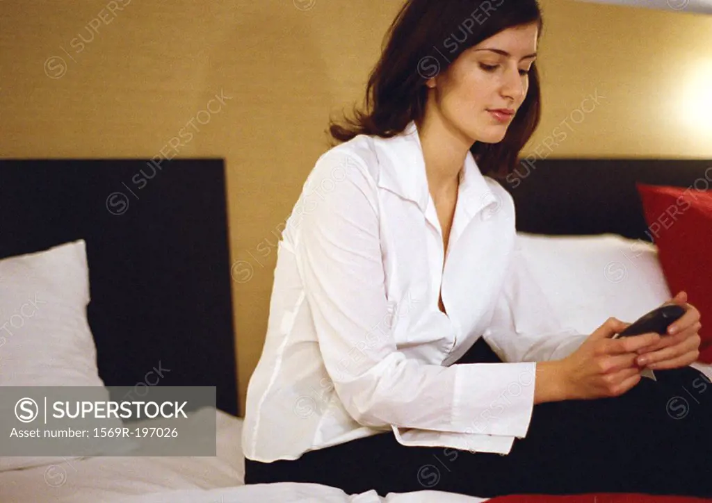 Businesswoman sitting on bed, using cell phone