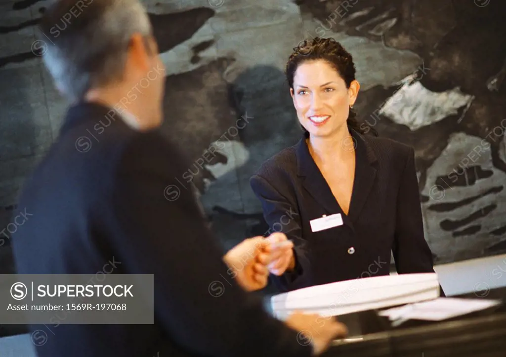 Woman behind counter smiling, handing object to man