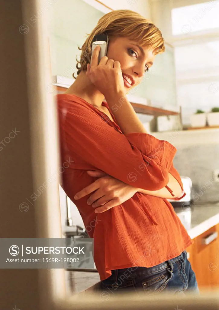 Young woman leaning against counter in kitchen, uisng cellphone