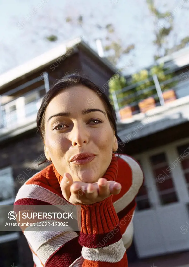 Woman leaning forward blowing a kiss, head and shoulders, close-up, house in background, low angle view
