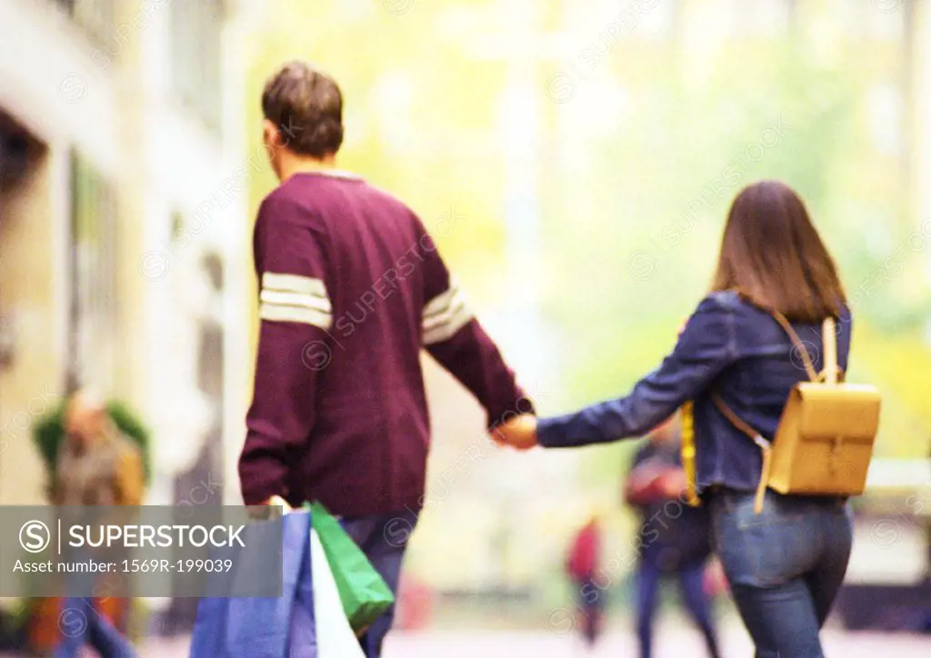 Couple shopping together, holding hands, view from behind