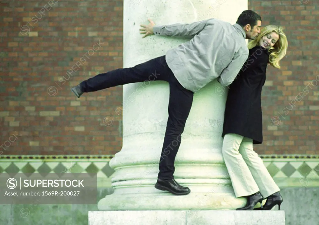 Man and woman standing on column, man stretching to kiss woman