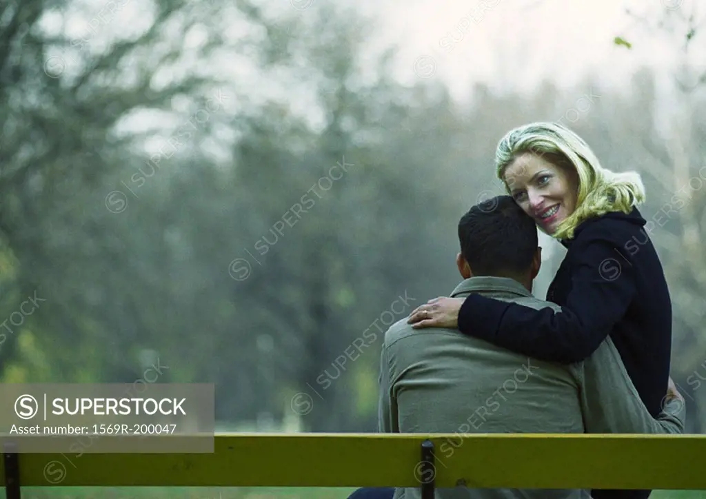 Man and woman sitting on bench, woman on his lap, view from behind