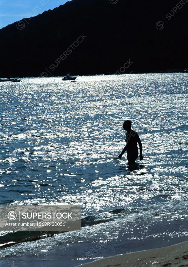 Person wading in sea, mountain in background