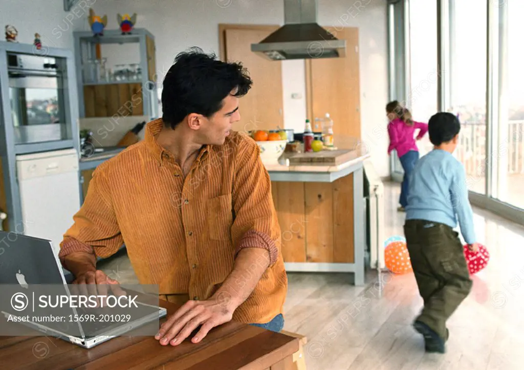 Father looking back at children playing with balls in the house