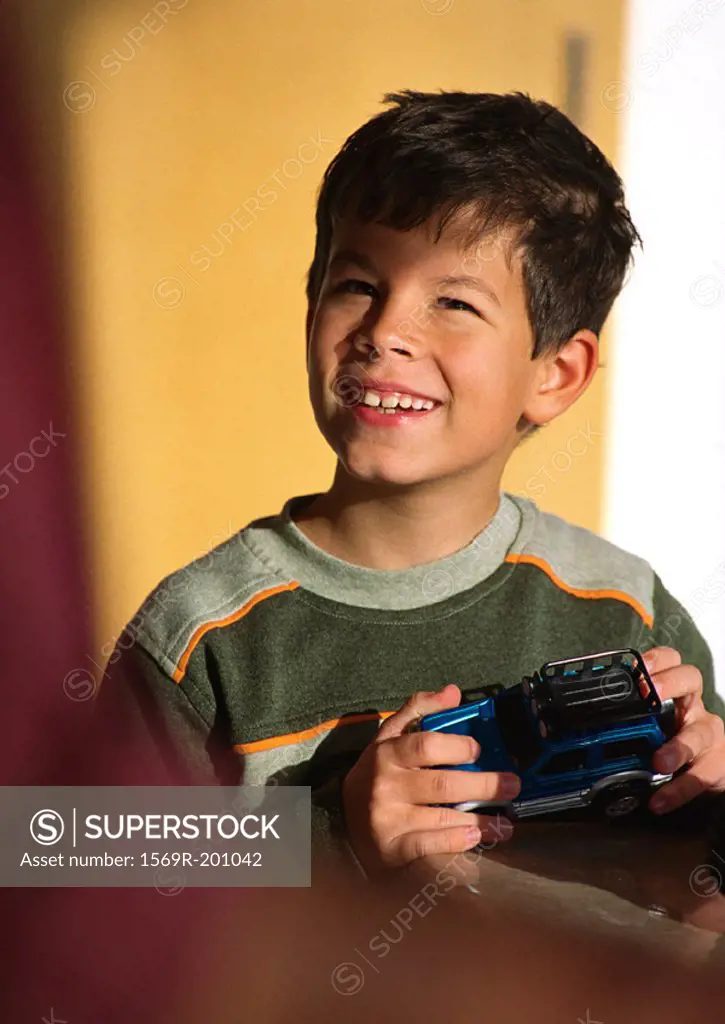 Child holding toy car, looking up