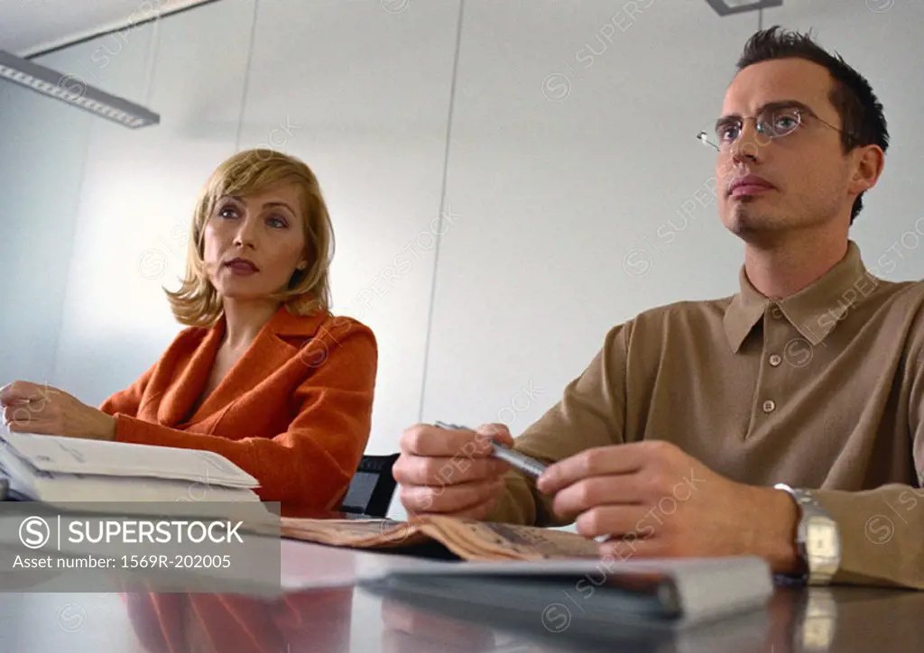 Businessman and businesswoman sitting at table next to each other