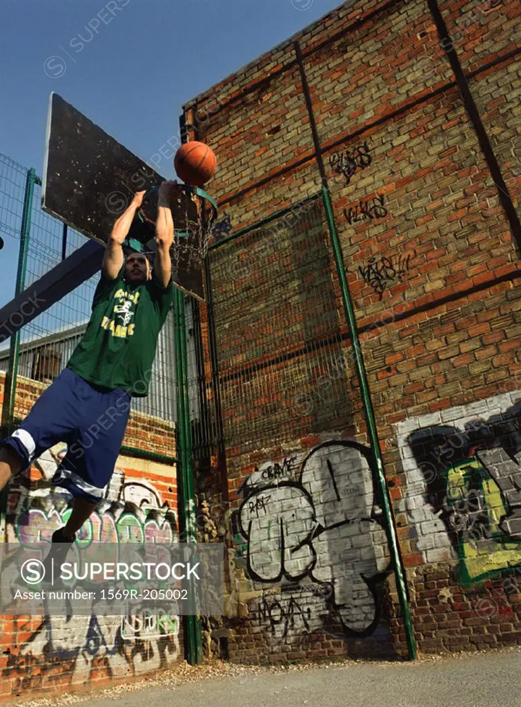 Man dunking basketball backwards in urban playground