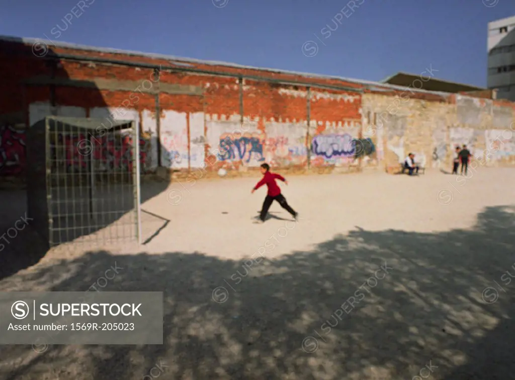 Person playing soccer on dirt yard next to graffiti wall