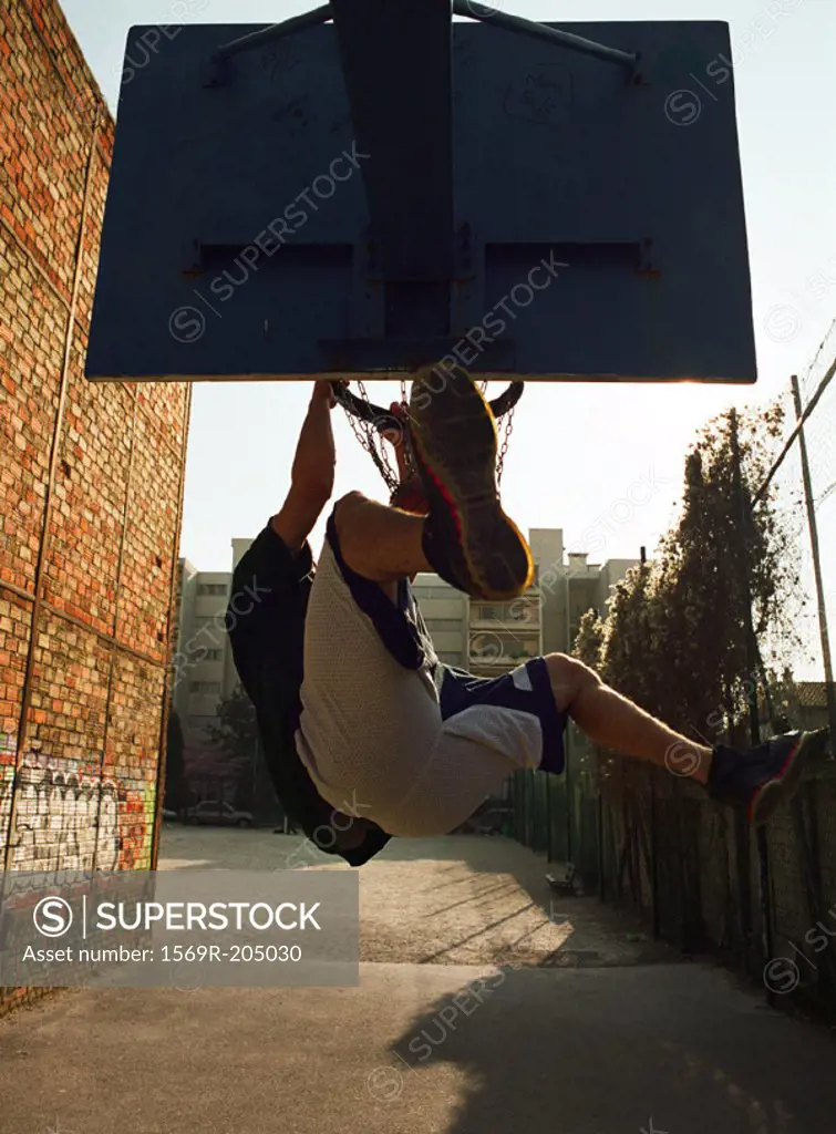 Man hanging on basketball rim after dunking ball, shot from behind