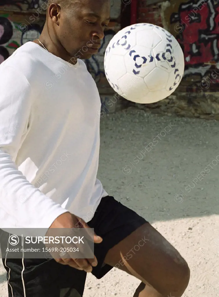 Man juggling soccer ball in front of graffitied wall