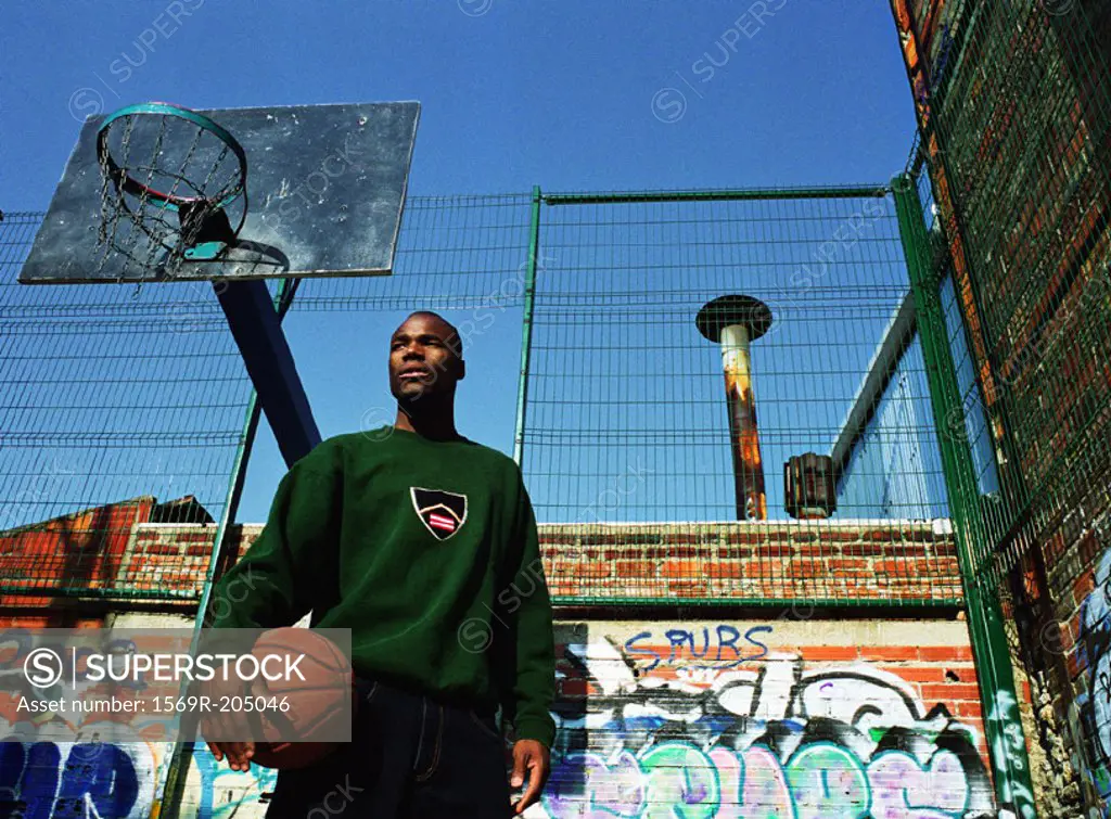 Man holding basketball in front of hoop and graffitied wall