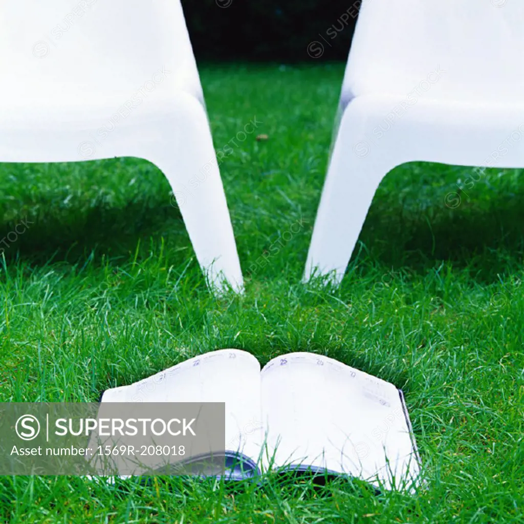 Book and two plastic chairs on grass