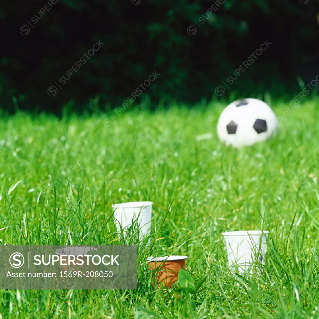 Paper cups and soccer ball in grass