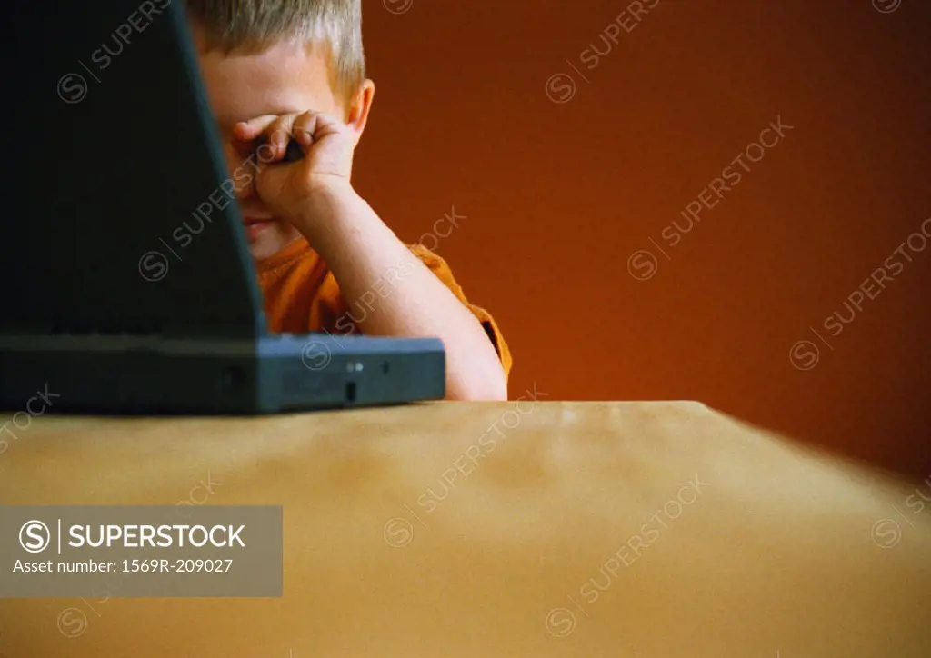 Little boy with laptop, rubbing eyes