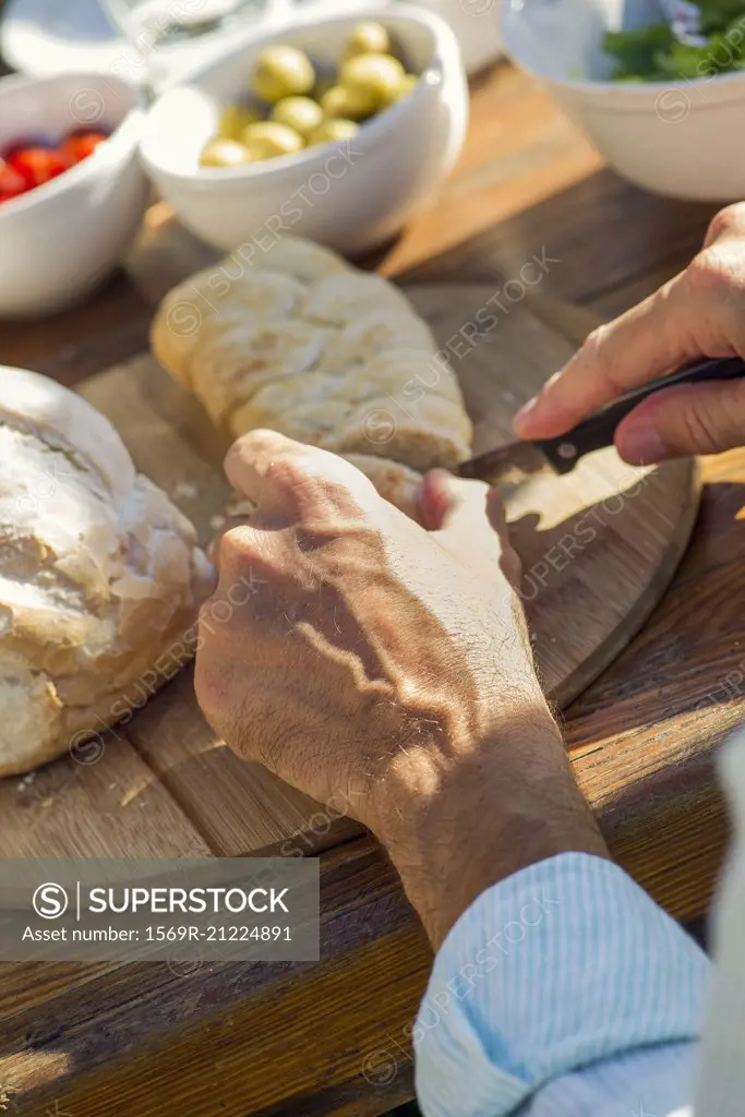 Man's hands cutting fresh loaf of bread outdoors