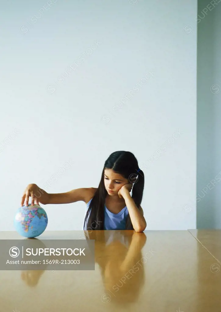 Girl sitting at table with hand on globe