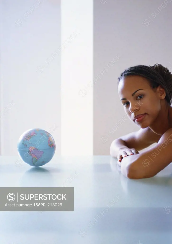 Woman with arms on table next to small globe, looking at table