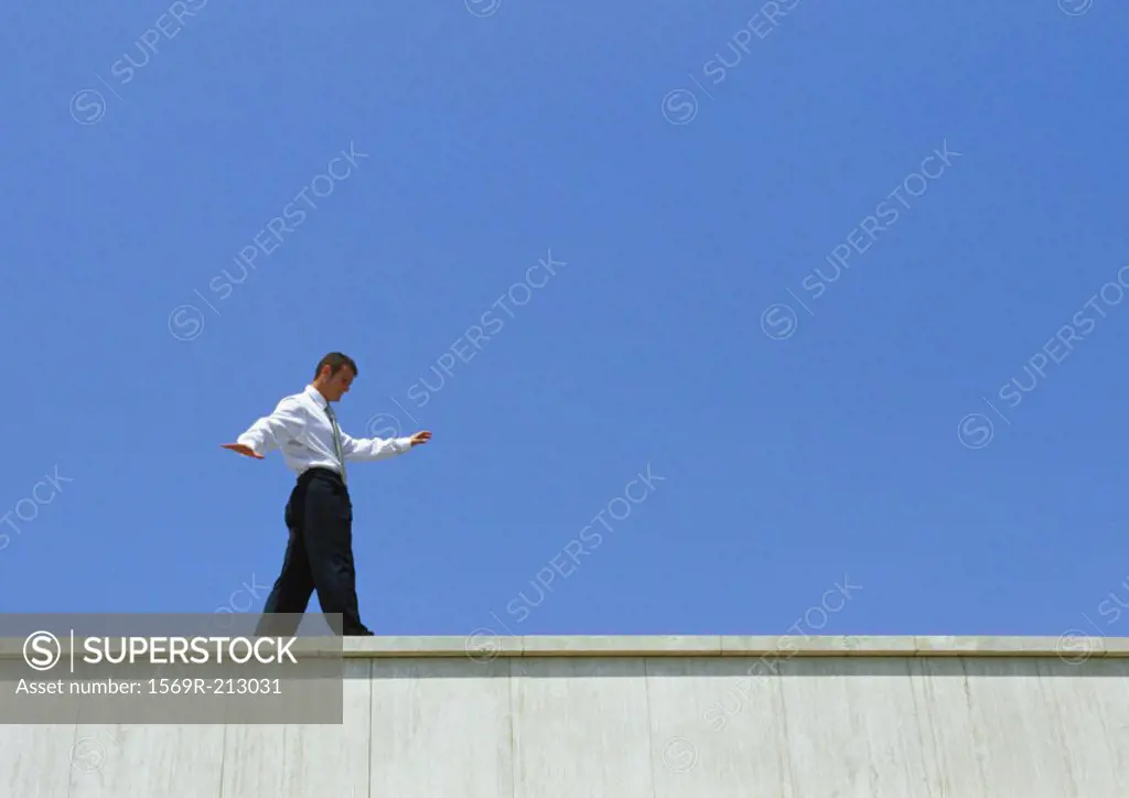 Businessman walking on edge of building, low angle view