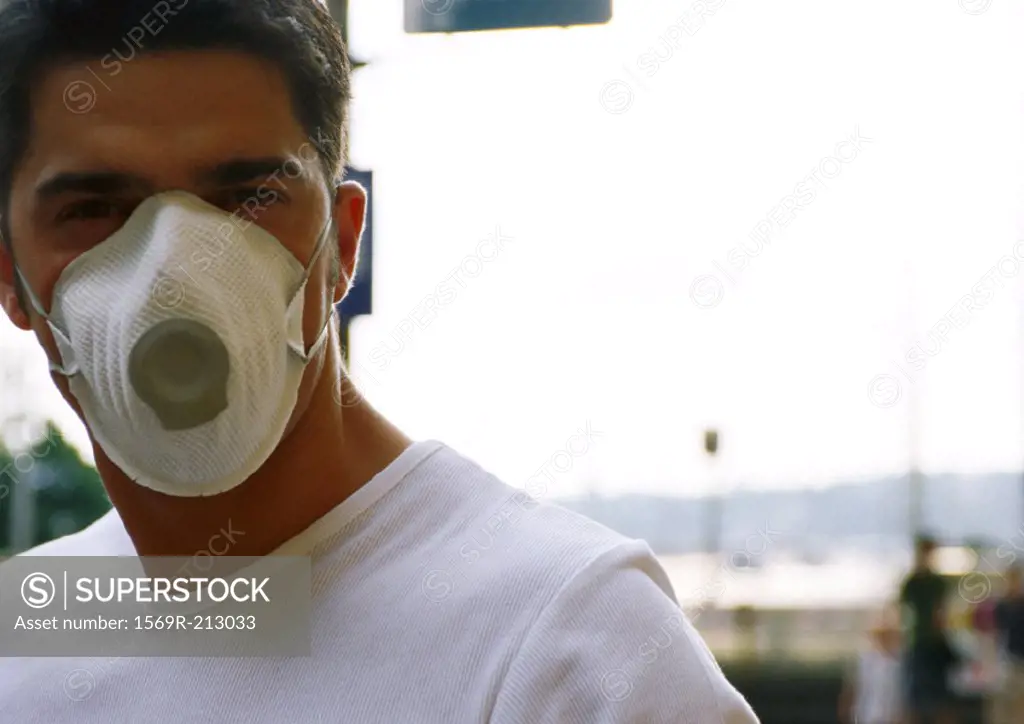 Man wearing white dust mask over nose and mouth, blurred background