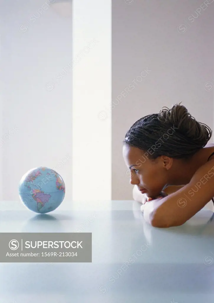 Woman staring at small globe, side view