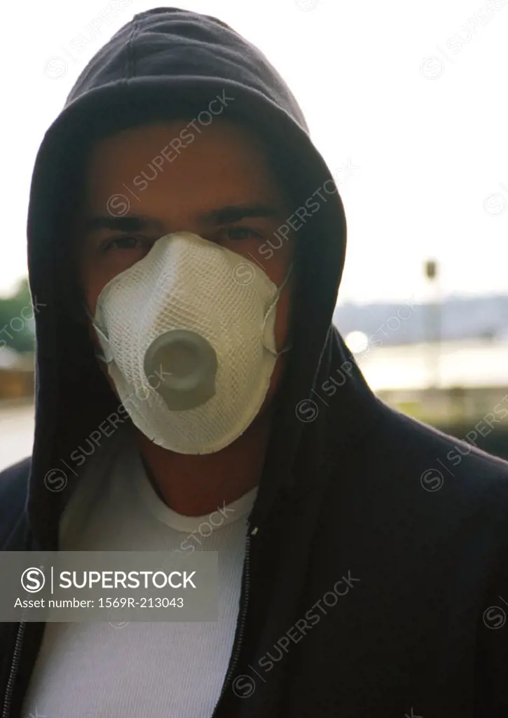 Man wearing hooded sweatshirt and white dust mask over nose and mouth