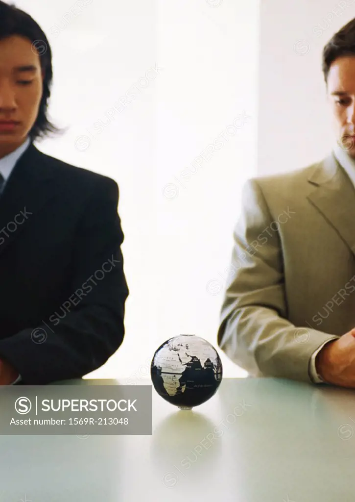 Two businessmen looking down at small globe on table