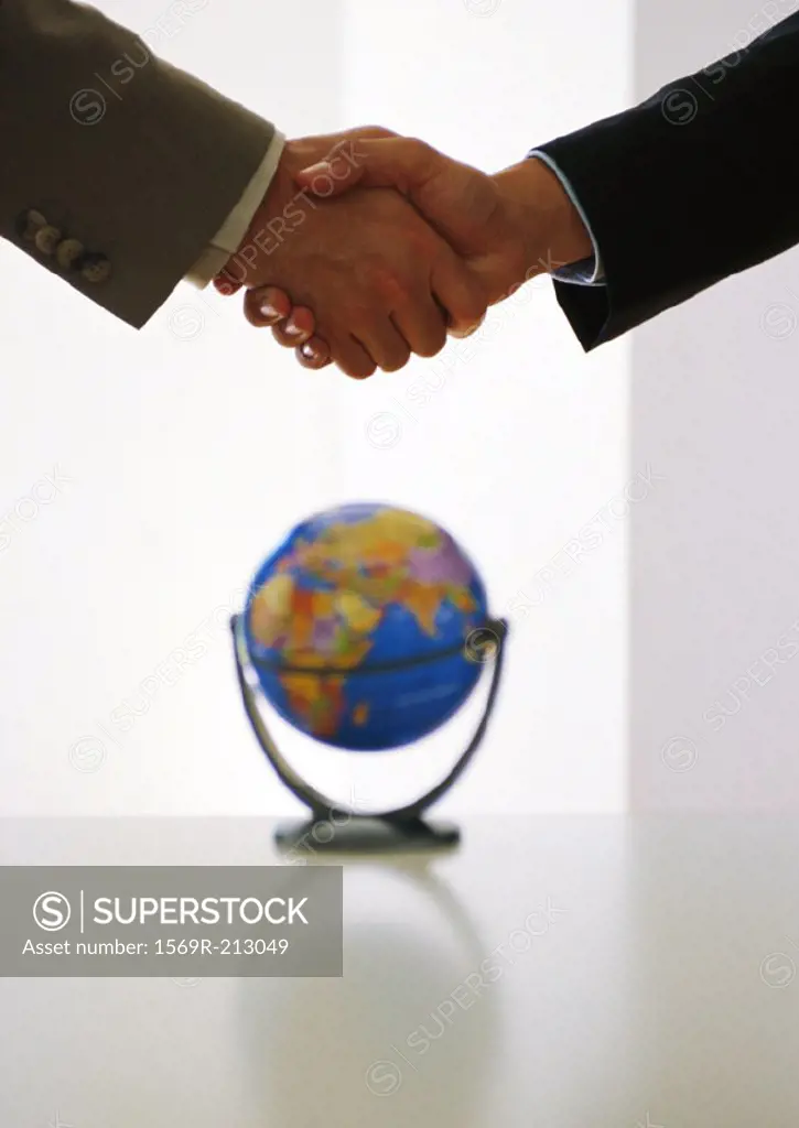 Two businessmen shaking hands above globe
