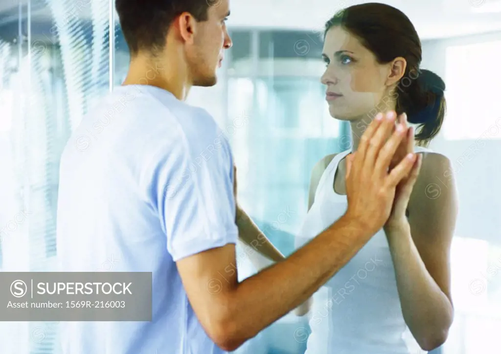 Couple, face to face, putting hands together on either side of glass wall