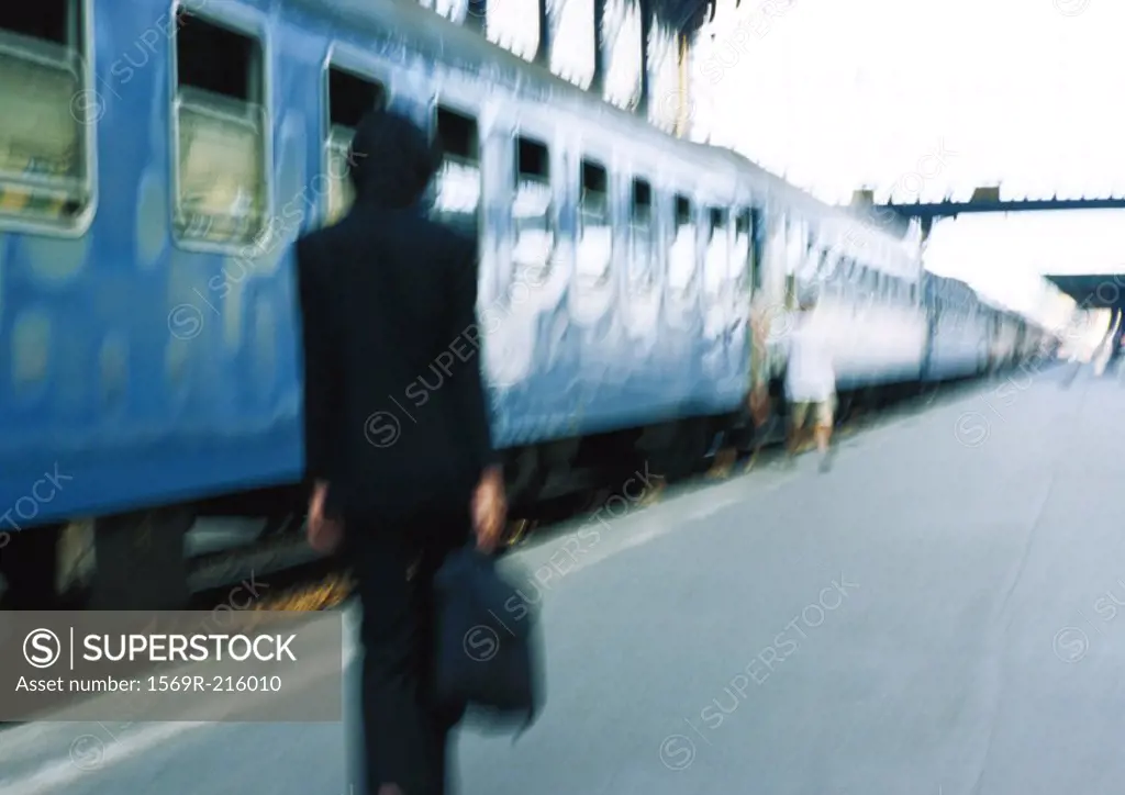 Businesswoman on platform next to train, rear view, blurred