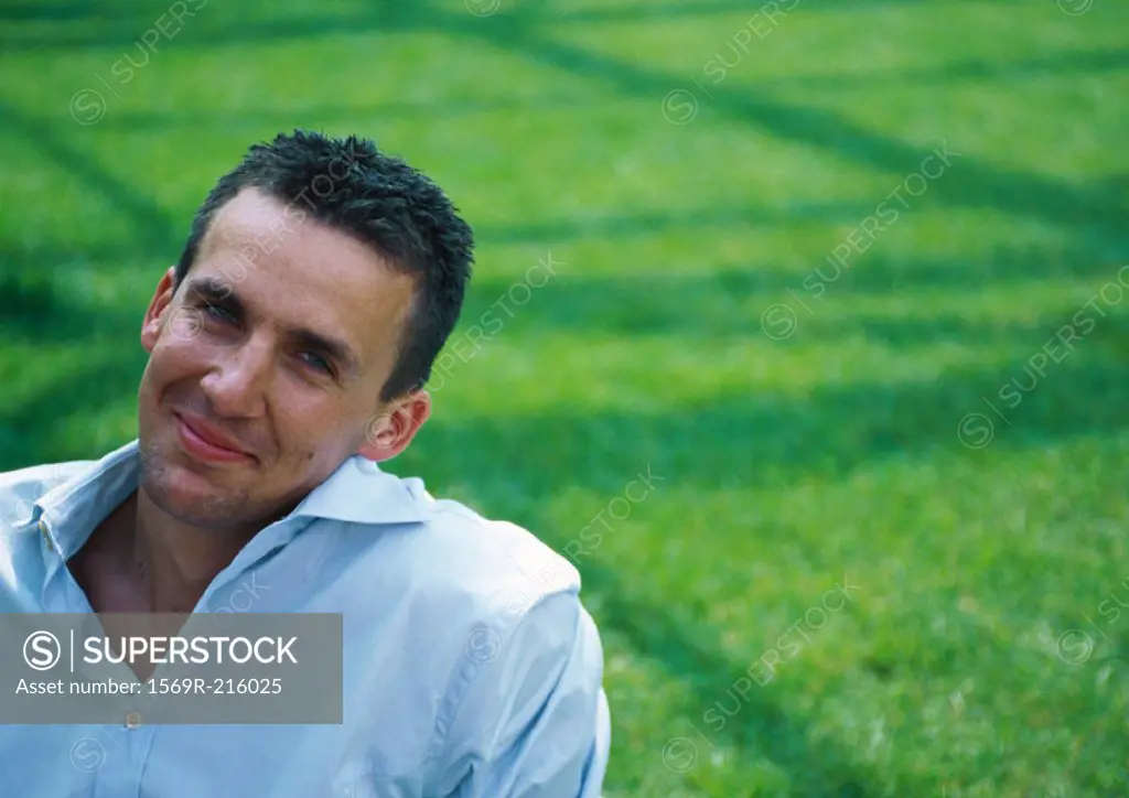 Man, head tilted, smiling at camera, green grass in background