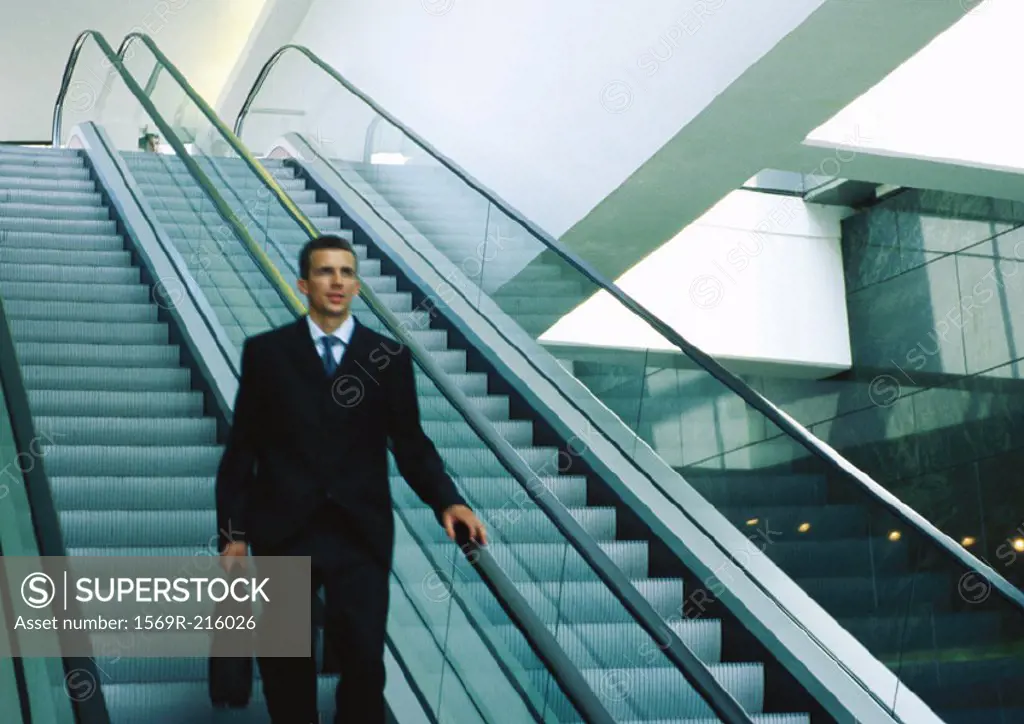 Businessman riding down escalator