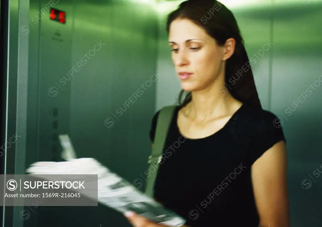 Woman reading newspaper in elevator