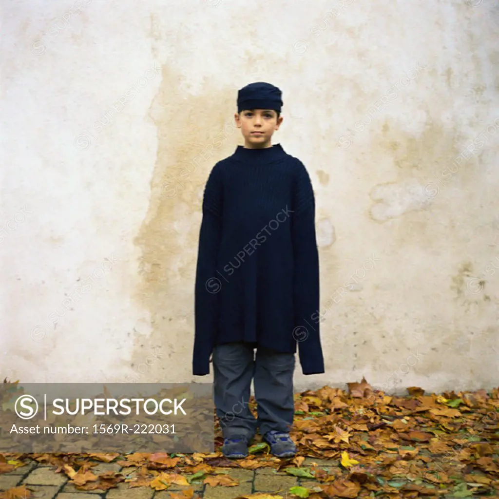 Boy standing among autumn leaves, wearing oversized sweater