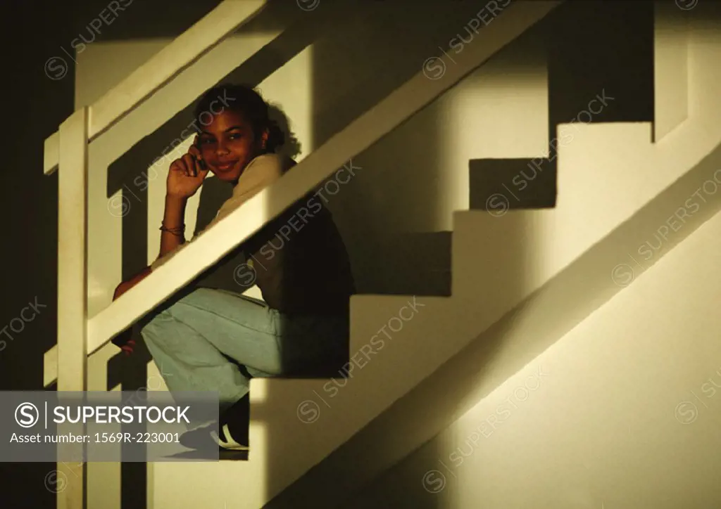 Young boy sitting on stairs, taklking on phone, smiling